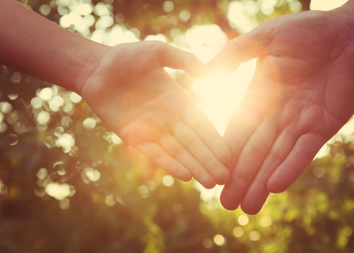 two hands creating heart in sunlight